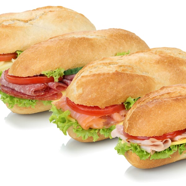 Four fresh submarine sandwiches with various fillings like salami, salmon, and ham on a white background.