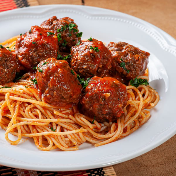 Spaghetti and meatballs with red sauce and parsley on a white plate from The Pizza Guyz.
