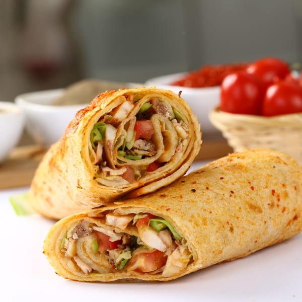 Two chicken wraps, cut in half, revealing chicken, lettuce, and tomatoes, with cherry tomatoes in the background.