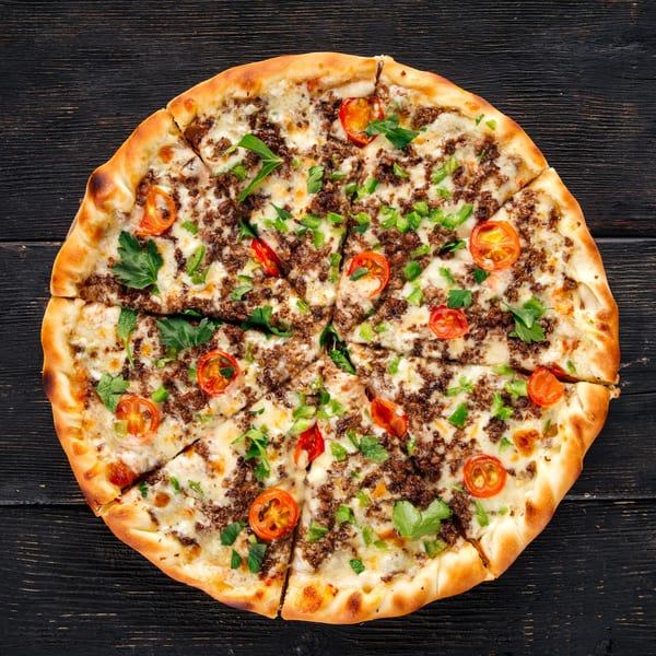 The Pizza Guyz's sliced pizza with ground meat, melted cheese, cherry tomatoes, and herbs.