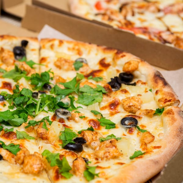 Close-up of a Pizza Guyz pizza with chicken, black olives, pineapple, and fresh parsley.