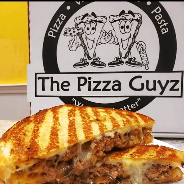 A grilled sandwich with melted cheese and meat filling, in front of a "The Pizza Guyz" box.